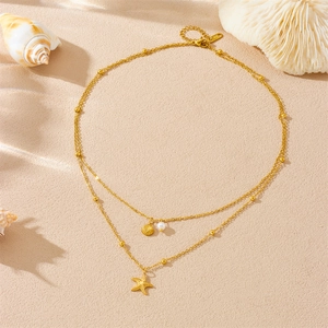 Gold double layer starfish and shell necklace with pearls on a beach sand background
