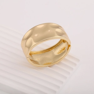 Macro detail of the wide gold hammered metal cuff bracelet with side hinge and textured finish