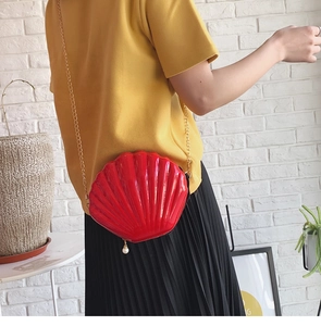 Detail of red shell-shaped crossbody bag with pearl pendant and gold chain on model
