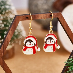 Close-up of penguin enamel earrings with red hats on a wooden display for Christmas