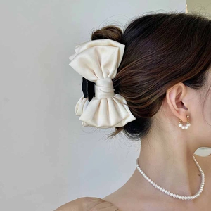 Detail of a large beige satin bow hair claw clip worn by a girl with elegant pearl jewelry