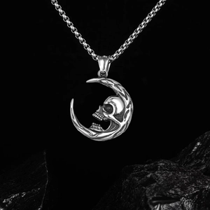 Detail of silver skull crescent moon pendant with box chain on dark rock texture