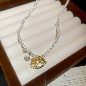 Close-up of white pearl necklace with golden rocking horse pendant in beige jewelry box