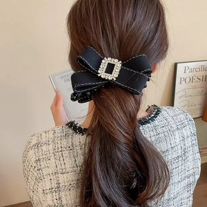 Detail of a black fabric bow hair clip with a crystal rhinestone buckle on brown hair