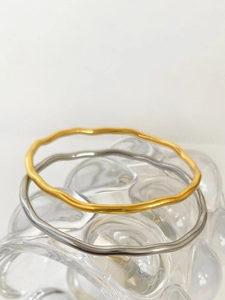 Close-up of stacked gold and silver wave-shaped titanium steel bracelets on glass base