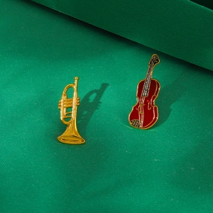 Detail of gold trumpet and reddish-brown violin enamel brooches on green textured surface
