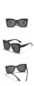 Detail view of large square cat-eye sunglasses with glossy black frame and grey lenses