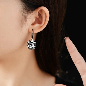 Close-up of leopard print round drop earrings worn on ear with black hoop accents