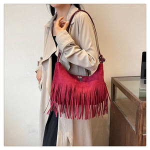 Détail du sac à bandoulière bordeaux à franges en daim porté sur un trench beige