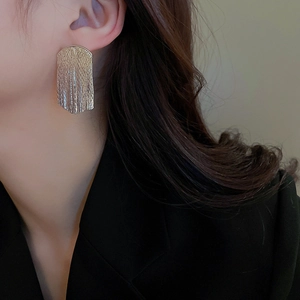 Close-up of golden geometric tassel earrings with textured surface on a model