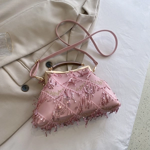 Detail of pink sequin clutch bag with tassel fringe and textured wooden handle on fabric