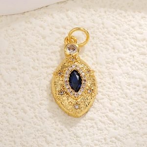 Macro detail of gold-plated oval pendant featuring blue stone and intricate relief design