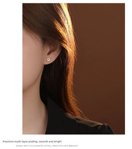 Close-up of silver coin stud earrings worn by a model in a warm textured setting