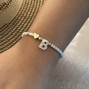 Close-up of white beaded bracelet with golden heart and letter B charm on wrist