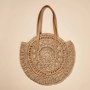Detailed close-up of woven hollow flower pattern on a round beige straw beach bag