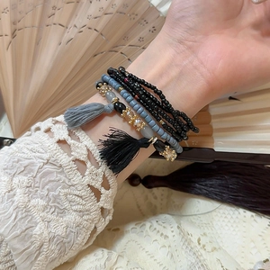 Detail of bohemian layered crystal bracelet with black tassels on lace and fan background