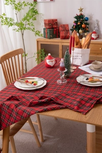 Close-up of red and green plaid Christmas tablecloth with tassels on a wooden dining table