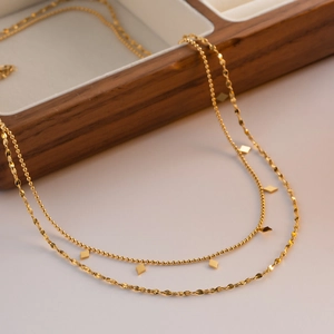 Double-layered gold fringe necklace with square charms on wooden box display