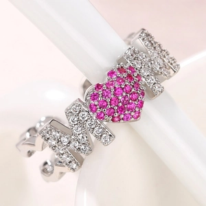 Close-up of MOM letter ring with pavé heart and zircons on a soft pink background