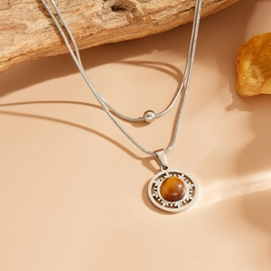 Détail d'un collier double chaîne serpent argentée avec pierre œil de chat brune sur bois