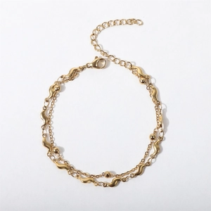 Detail of double-layer gold chain bracelet with irregular wave links and polished beads