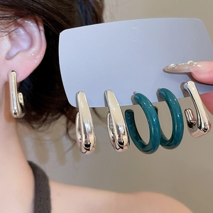 Detailed view of silver U-shaped hoop earrings and dark green resin round earrings
