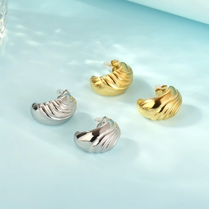 Detailed view of gold and silver textured earrings with wavy patterns on a blue water surface