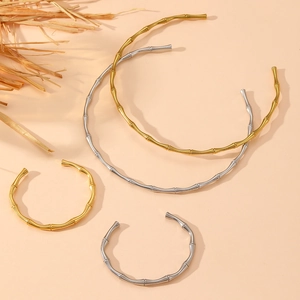 Set of four bamboo-shaped open bangles in gold and silver finish on a beige background