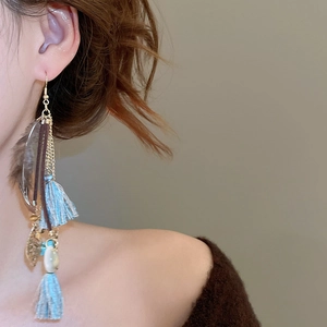 Close-up of bohemian blue fringe earrings with golden leaf charm on model's ear