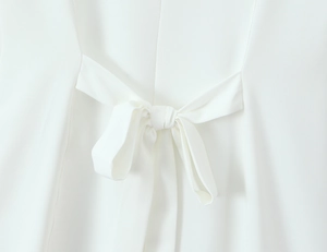 Detailed close-up of the delicate white lace mini dress featuring a stylish back bow tie