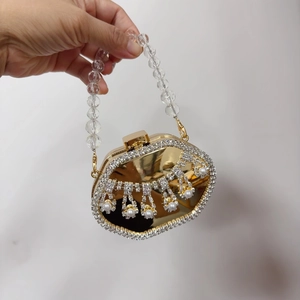 Detailopname van een luxe gouden mini-avondtas met strassteentjes en elegante parels