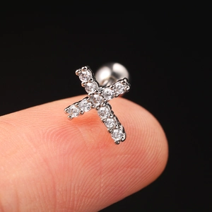 Macro shot of a tiny silver cross stud earring with sparkling zircons held on a finger