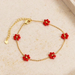 Detail of gold chain bracelet with red floral beads and heart pendant on beige linen