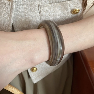 Detailed view of a wide acrylic marble texture bangle worn with a tweed jacket