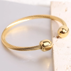 Close-up of golden cable wire bracelet with polished sphere ends on a textured stone