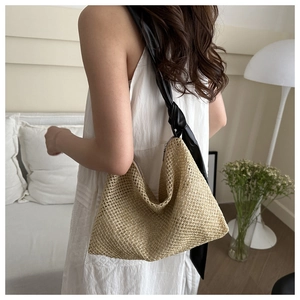 Close-up of beige woven straw shoulder bag featuring elegant black satin bow straps