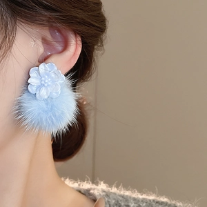 Detail of light blue floral resin and fluffy fur ball earrings worn by a model