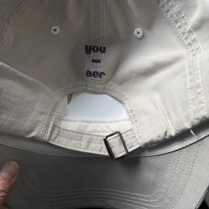 Détail d'une casquette beige avec broderie violette et boucle de réglage en laiton