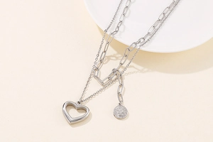 Close-up of double-layer silver necklace with heart and coin pendants on beige background