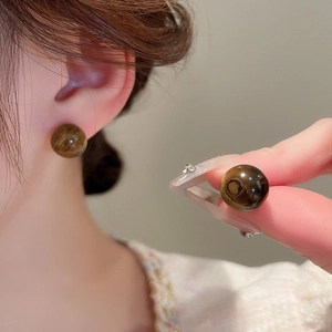 Close-up detail of a model wearing brown spherical tiger eye stud earrings with gold plating