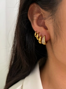Gros plan d'une femme portant des créoles dorées et un clou d'oreille en forme de goutte