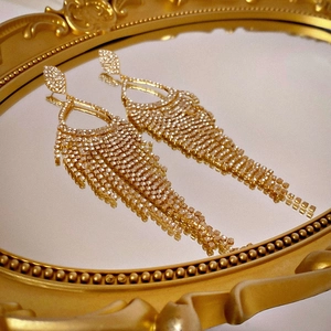Close-up of golden tassel earrings with rhinestones on a vintage mirrored tray