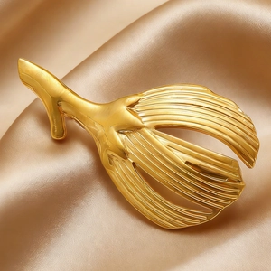Detailed close-up of golden ginkgo leaf brooch with fine brushed texture on satin