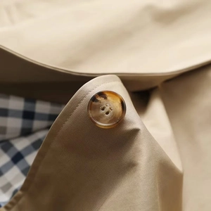 Detail eines beigen Trenchcoats mit Schildpatt-Knopf und blau-weiß kariertem Futter
