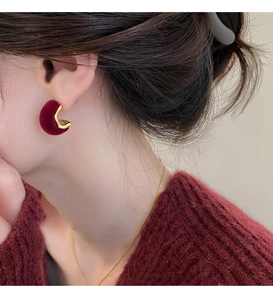 Detail of vintage burgundy velvet C-shaped stud earrings worn by a model in warm light
