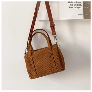 Close-up of brown corduroy Boston bag with front pocket and canvas strap on white wall