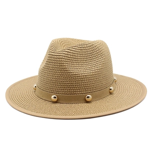 Detailed close-up of woven straw fedora hat with a band featuring golden metal rivets