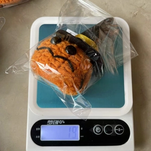 Macro shot of a crochet Halloween pumpkin toy showing weight of 19g on a digital scale