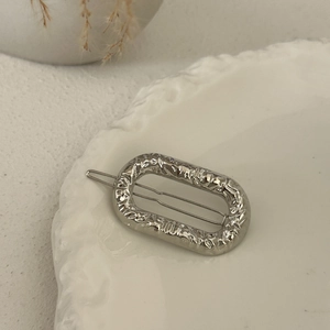 Close-up of a silver hammered metal oval hair clip on a white decorative ceramic plate