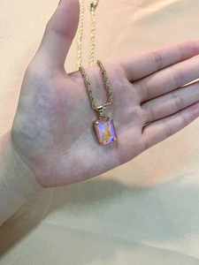 Detail of pink rectangular zirconia pendant with golden twisted rope chain on silk background